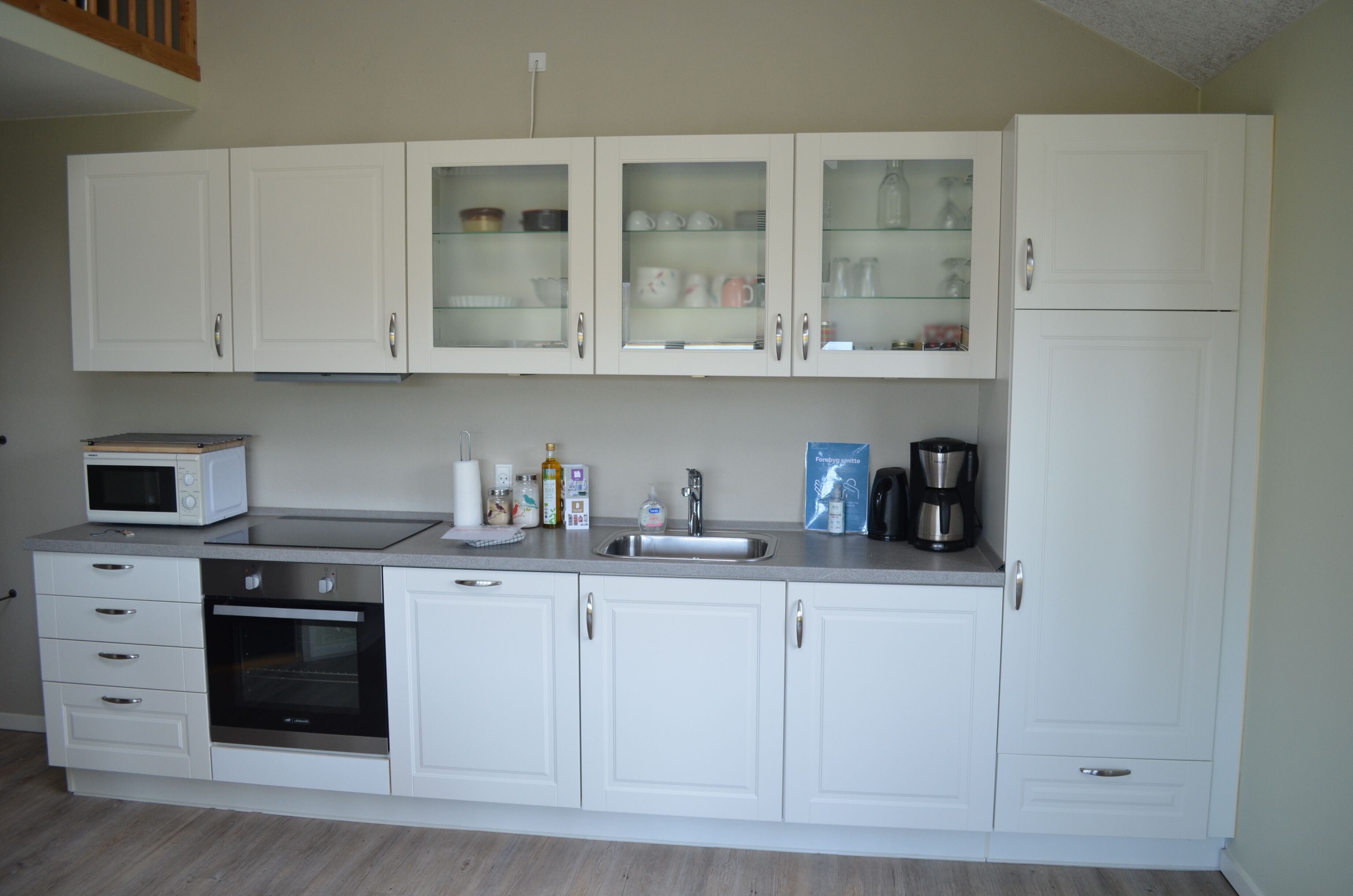 A modern kitchen with white cabinets, a microwave, an oven, and a coffee maker.