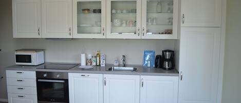 A modern kitchen with white cabinets, a microwave, an oven, and a coffee maker.