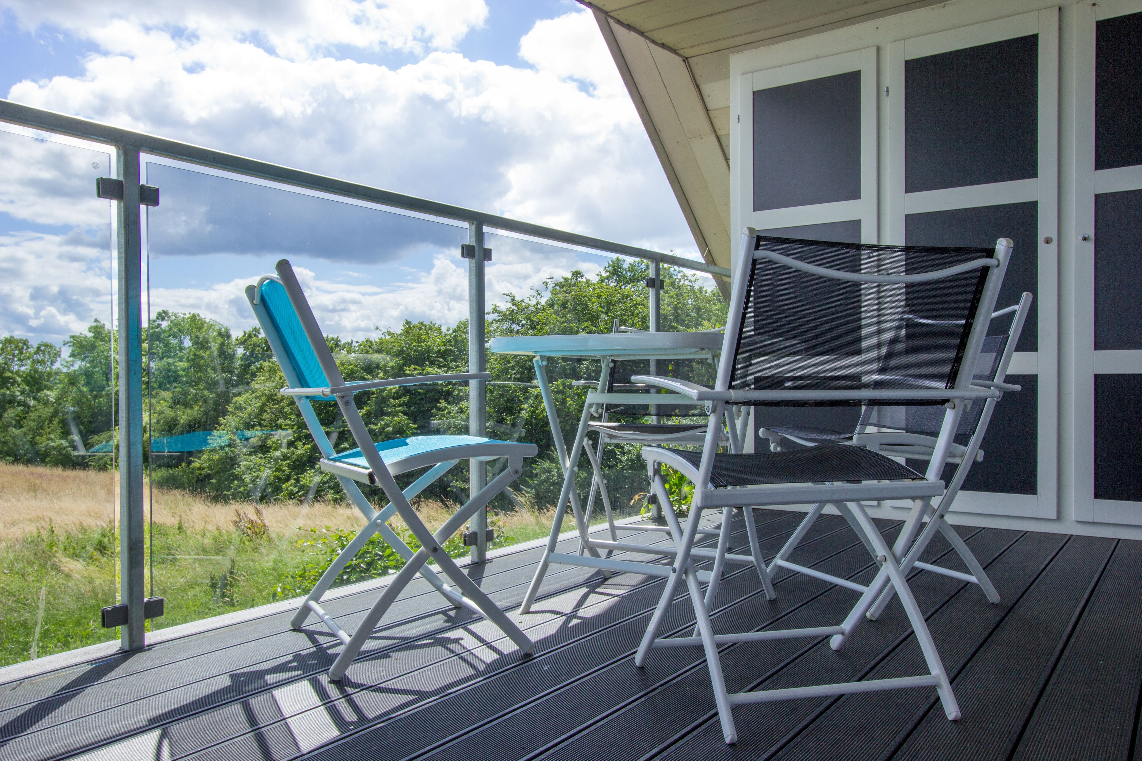 A balcony with a table and chairs, overlooking a grassy area and trees.