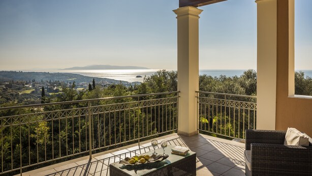 A balcony with a view of a coastal landscape, a wicker sofa, and a table with a tray of lemons and glasses. - Private pool and sea view (Leivathou)