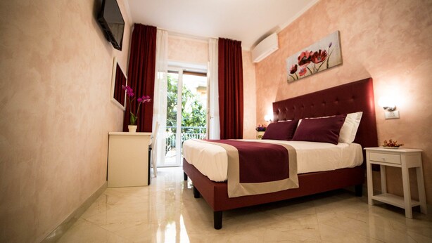 A hotel room with a bed, a nightstand, a desk, a painting, and a view of the outdoors. - St. Peter Area Luxury Suites (Rome)