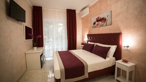 A hotel room with a large bed, a bedside table, a TV mounted on the wall, and a window with curtains. - St. Peter Area Luxury Suites (Rome)
