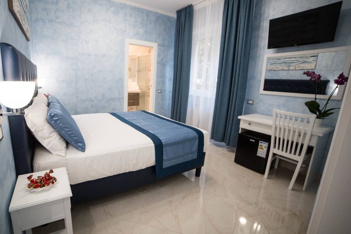 A bedroom with a bed, bedside table, dresser, and a desk with a chair.