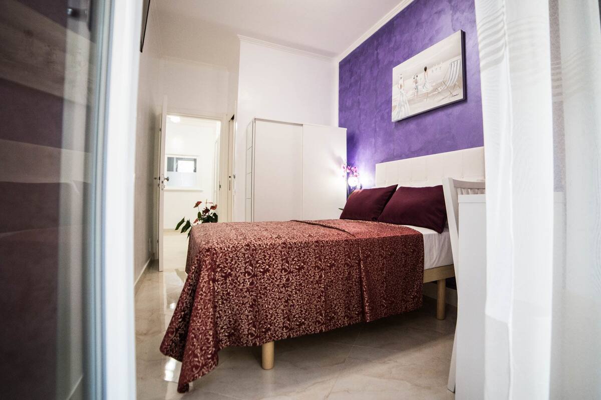A bedroom with a bed, a nightstand, and a wall-mounted painting.