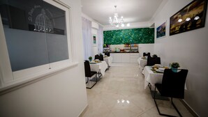 A dining area with white tables and chairs, a kitchen in the background, and a green leafy mural on the wall. - St. Peter Area Luxury Suites (Rome)