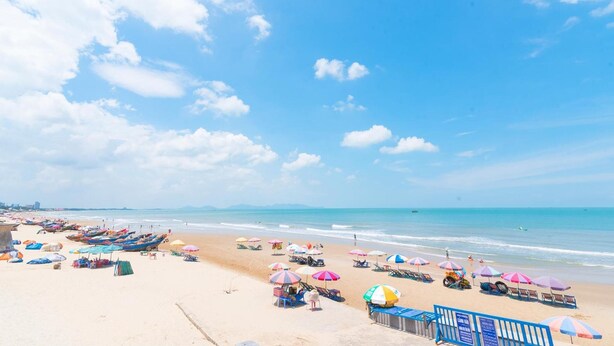 Una playa con hileras de sombrillas de colores y sillas de descanso, un cielo azul despejado y mar tranquilo.