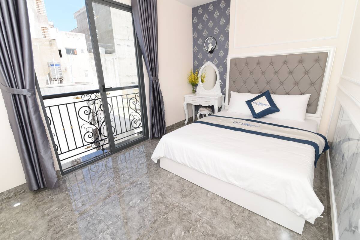 A hotel room with a bed, a vanity with a mirror, and a balcony with a view of buildings.