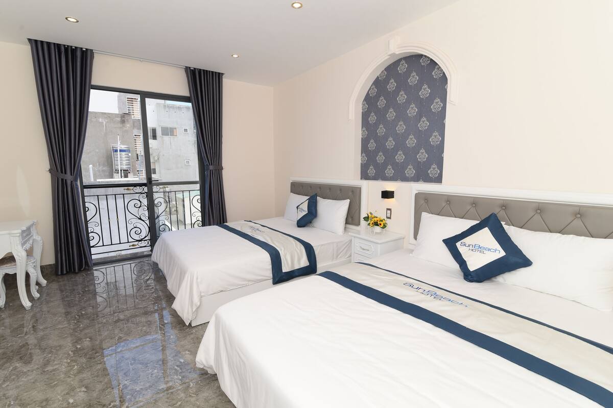 A hotel room with two beds, a balcony, and a view of the cityscape.