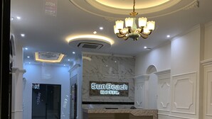 Zona de recepción de un hotel con suelo de mármol, una lámpara de araña y mostrador de recepción.