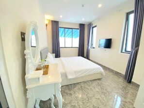 Habitación de hotel con una cama, tocador con espejo, televisor de pantalla plana montado en la pared y ventana con cortinas.
