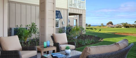 A covered outdoor seating area with wicker furniture and a view of a golf course.