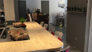 Een ruime eethoek met een lange houten tafel, gestreept beklede stoelen en diverse planten.