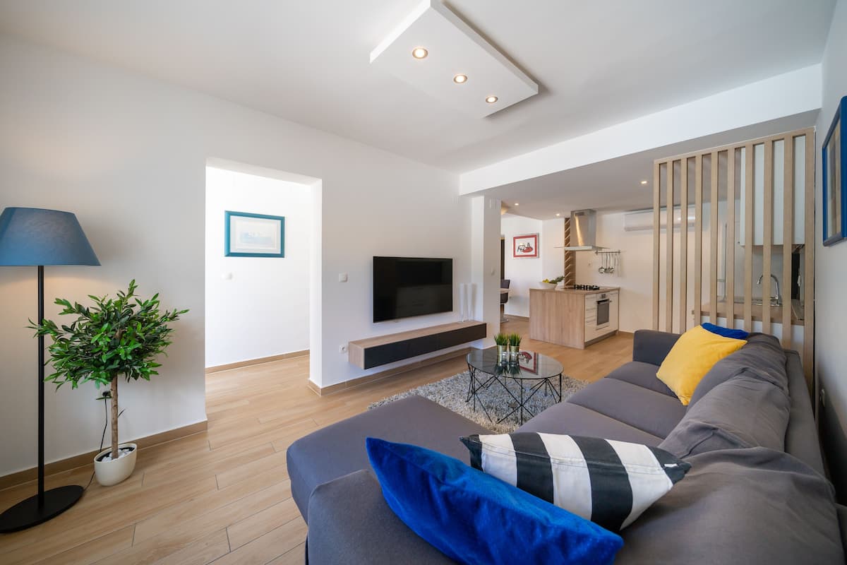 Uma sala de estar moderna com um sofá, uma televisão, uma planta e um abajur.