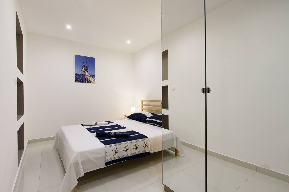 Quarto moderno com cama, mesa de cabeceira, espelho e quadro na parede.