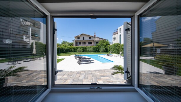 A modern building with a large window overlooking a swimming pool and a patio area. - Holiday Home Apartments Bellamare (Zadar)