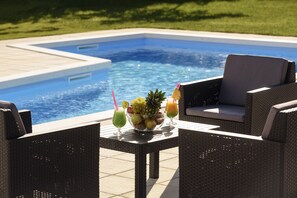 A poolside setting with wicker furniture, a fruit bowl, and two drinks.