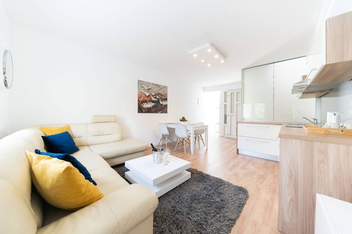 Uma sala de estar moderna com sofá, mesa de centro e uma área de refeições com cadeiras.