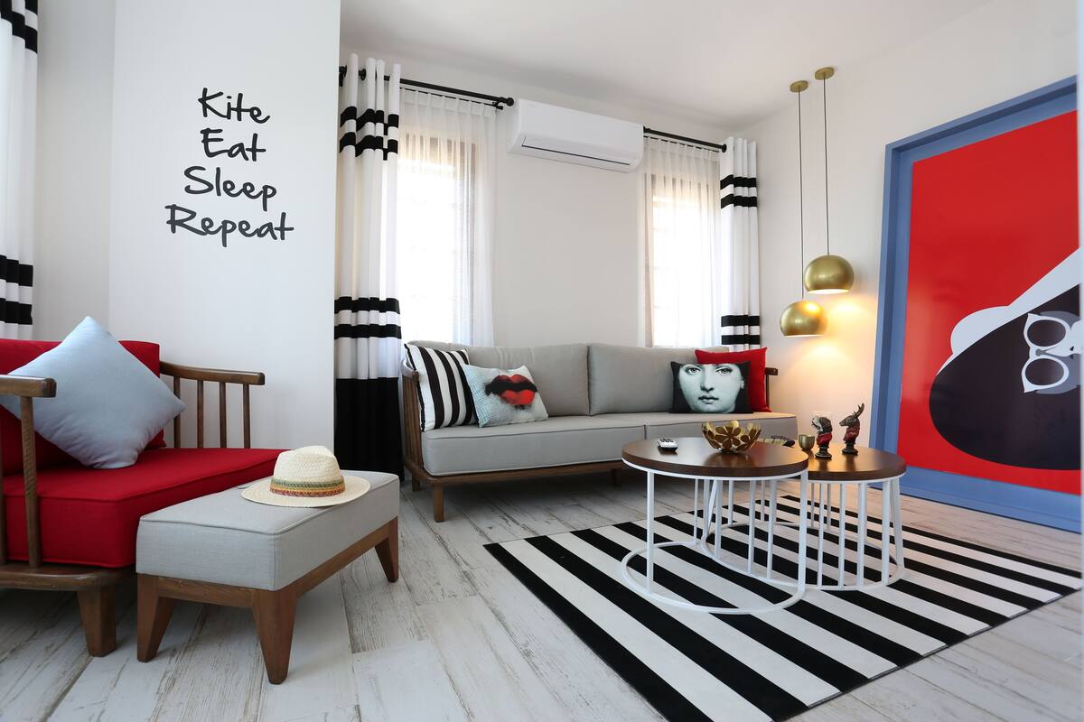 Uma sala de estar moderna com um sofá, uma poltrona vermelha, uma mesa pequena e um tapete listrado em preto e branco.