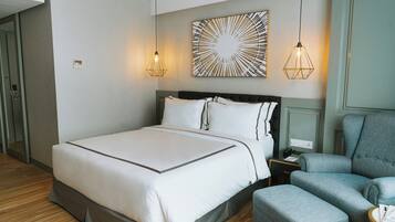 A modern hotel room with a large bed, a grey armchair, and a small table.