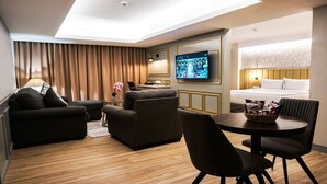 Una habitación de hotel moderna con sofá, sillón, mesa de comedor y televisor montado en la pared.