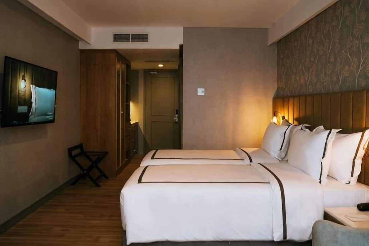 A hotel room with two beds, a television, a desk, and a chair.