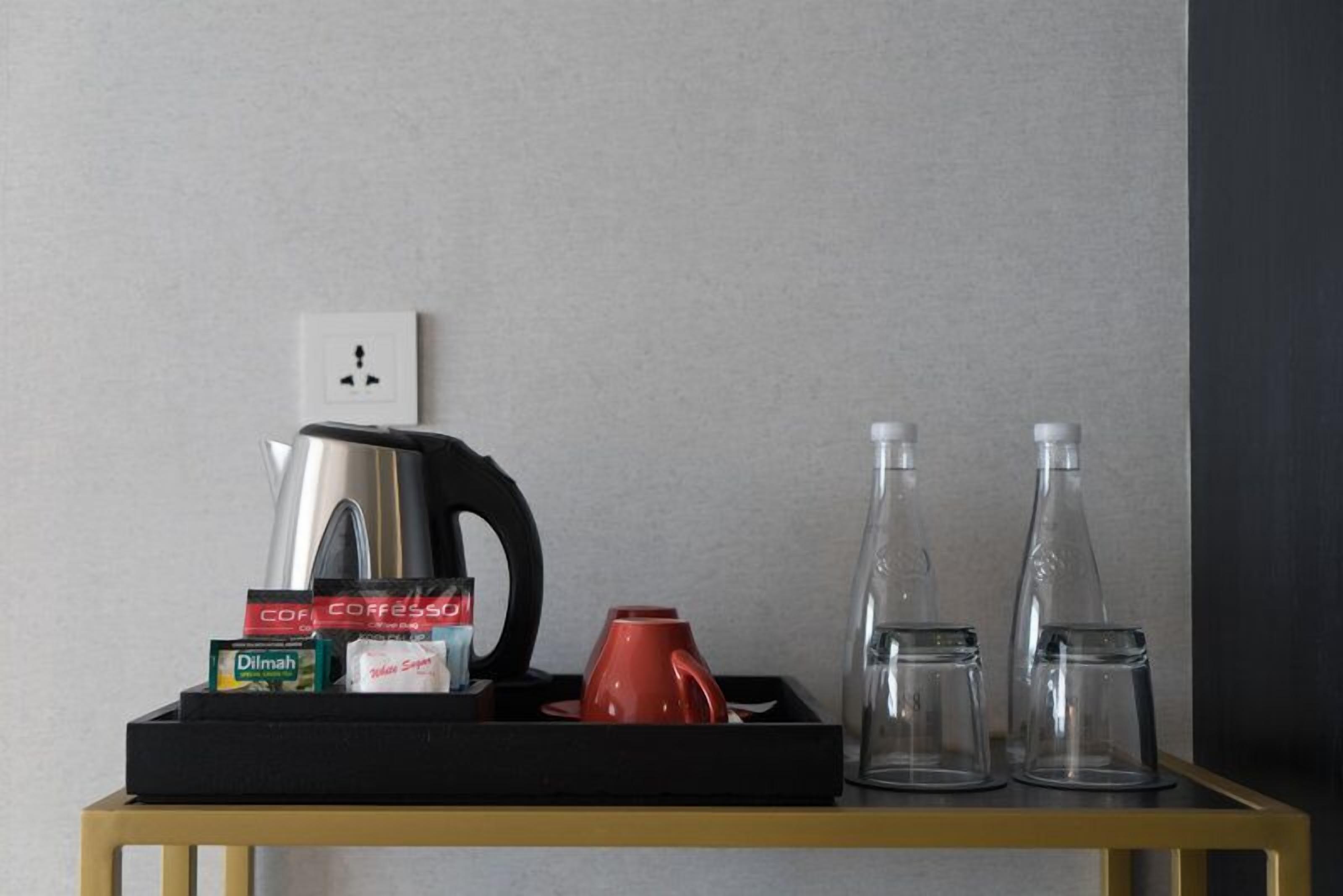 A tray with a coffee maker, coffee pods, a red mug, and two empty glass bottles on a table.