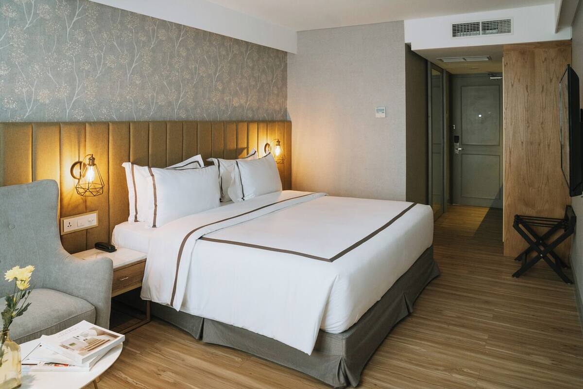 A hotel room with a large bed, bedside lamps, a chair, and a small table with a vase of flowers.