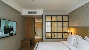 Habitación de hotel con una cama grande, televisor montado en la pared y ventana con vista al baño.