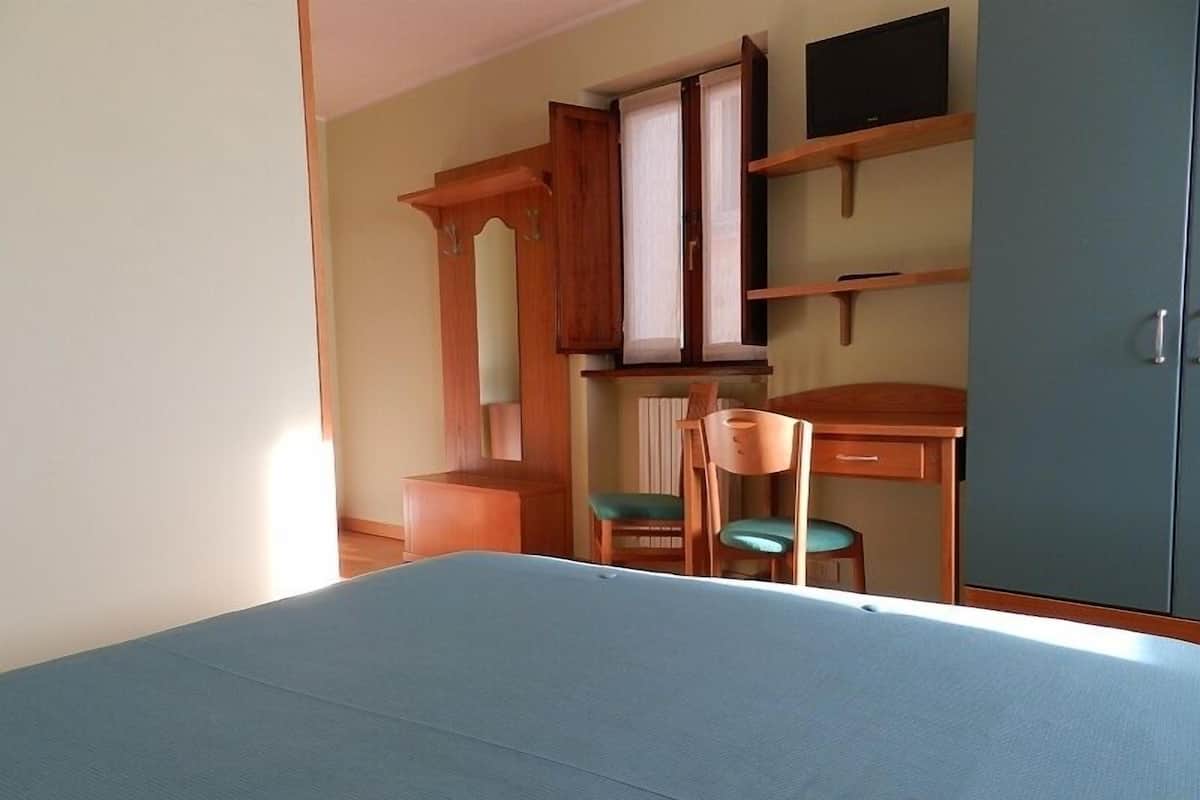 A room with a bed, a desk, two chairs, a wardrobe, and a television.