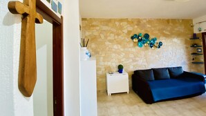 Una sala de estar con pared de piedra, un sofá azul, una mesita auxiliar blanca y una cruz de madera.