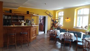 Un restaurante con zona de bar, sillas de madera y una mesa preparada para comer.