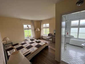 A bedroom with a bed, a desk, a chair, and a bathroom with a sink and window. - Spreewaldhotel Leipe (Lübbenau/Spreewald)