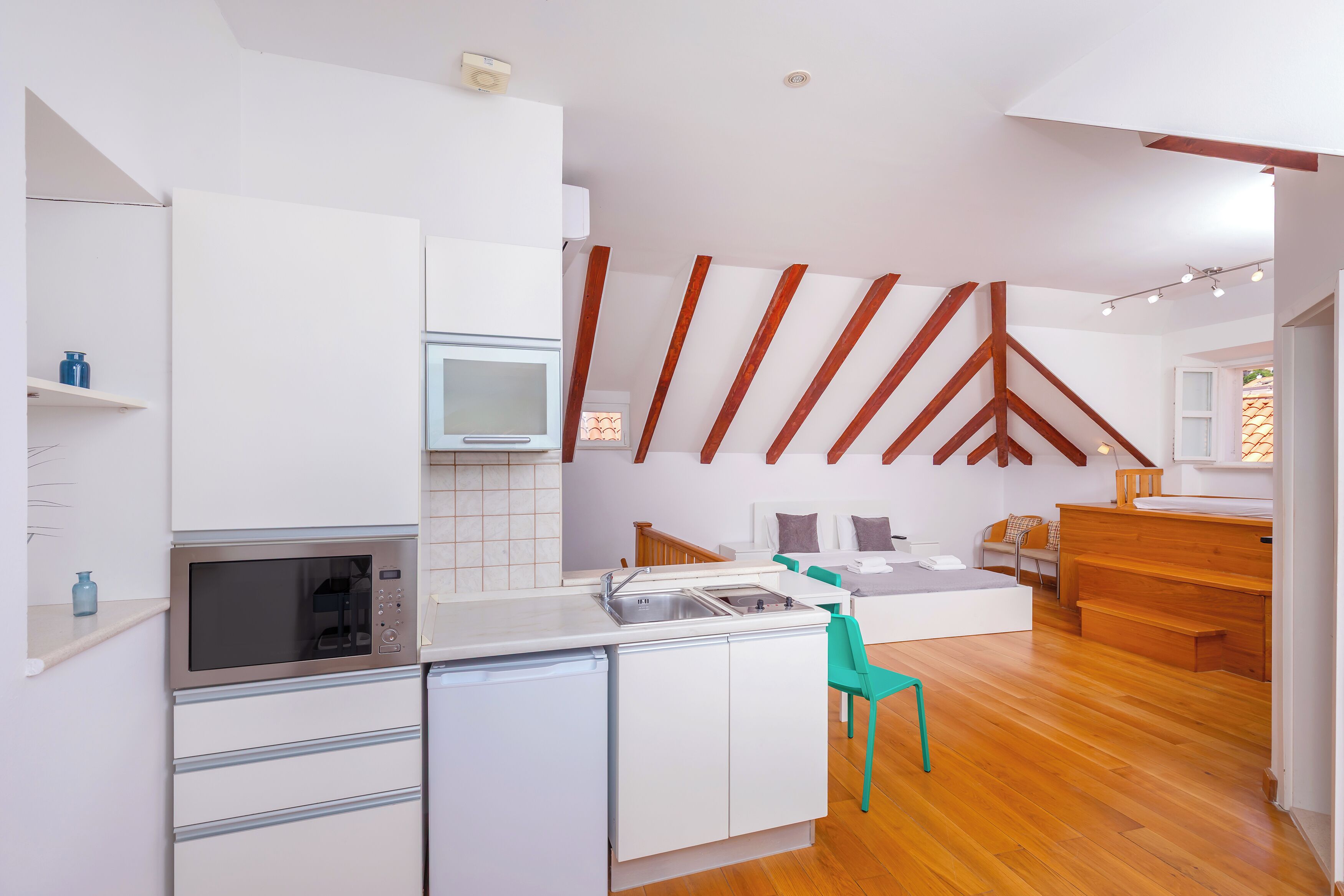Una cocina moderna con armarios blancos, un microondas integrado y una escalera de madera que conduce a una zona en loft.