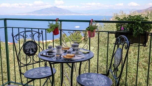 Une terrasse avec une table dressée pour le petit-déjeuner, offrant une vue panoramique sur un plan d’eau et des montagnes.