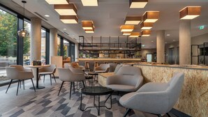A modern bar area with seating and a high ceiling with geometric light fixtures. - Holiday Inn - the niu, Timber Esslingen by IHG (Esslingen)