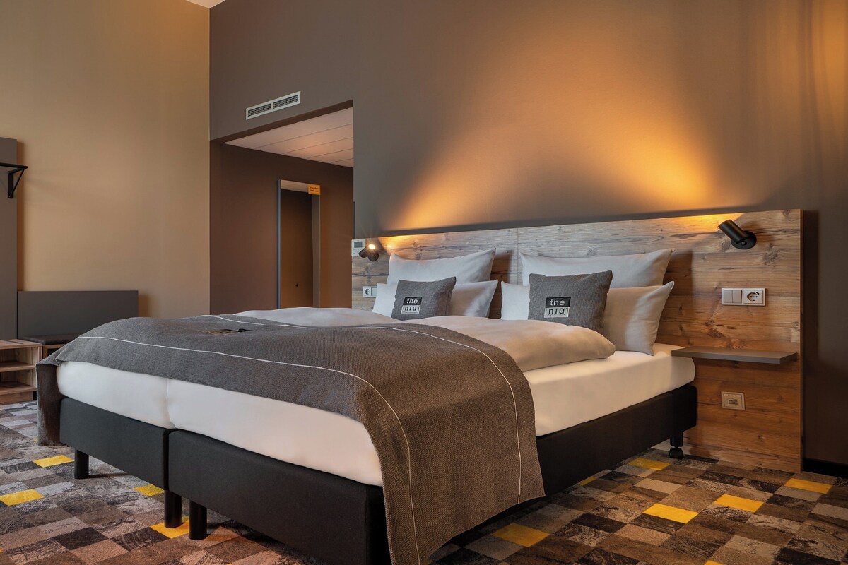 A modern bedroom with a large bed, a wooden headboard, a bedside table, and a checkered floor.