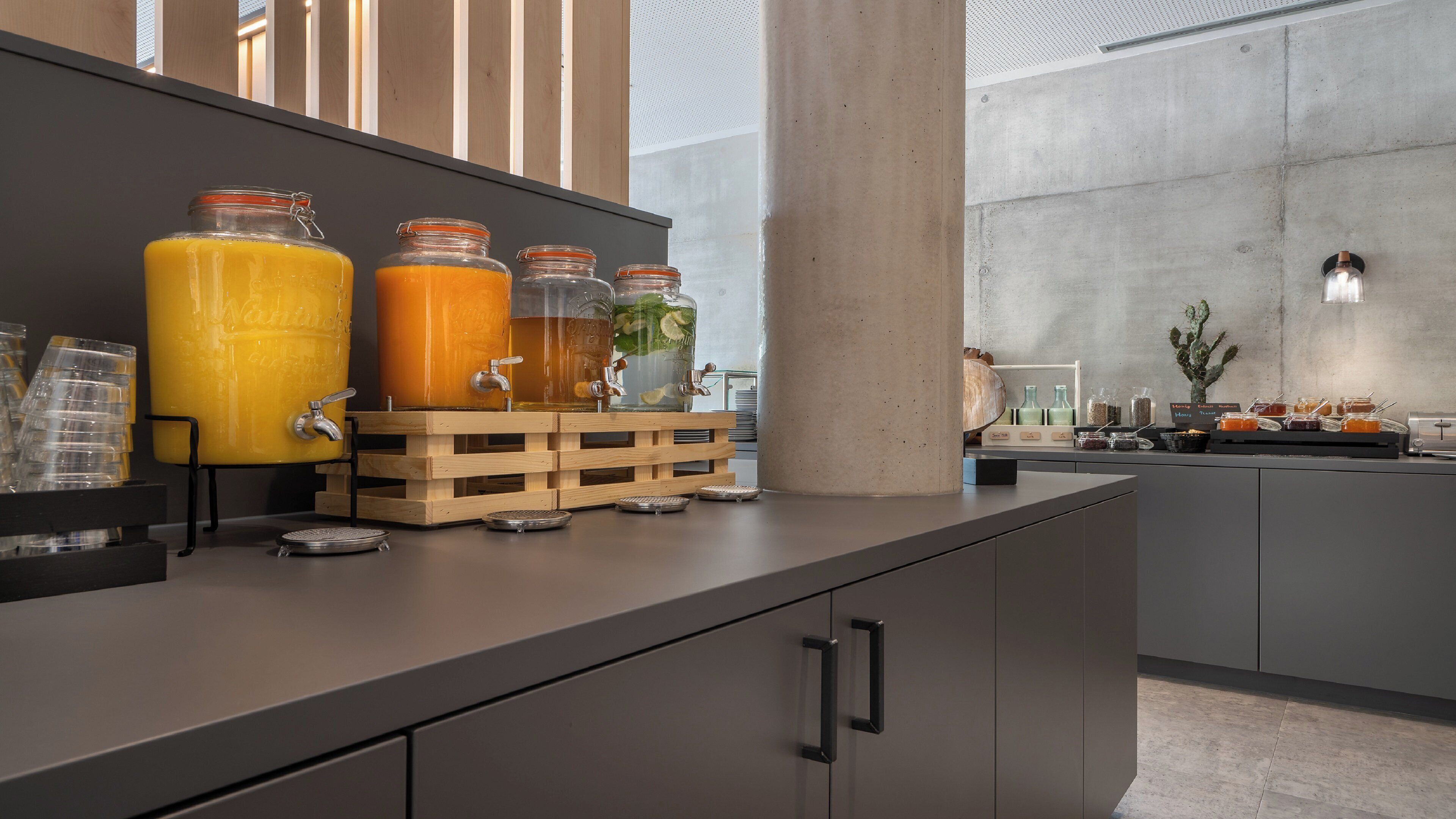 A modern kitchen area with a juice station featuring multiple glass dispensers and a wooden crate.