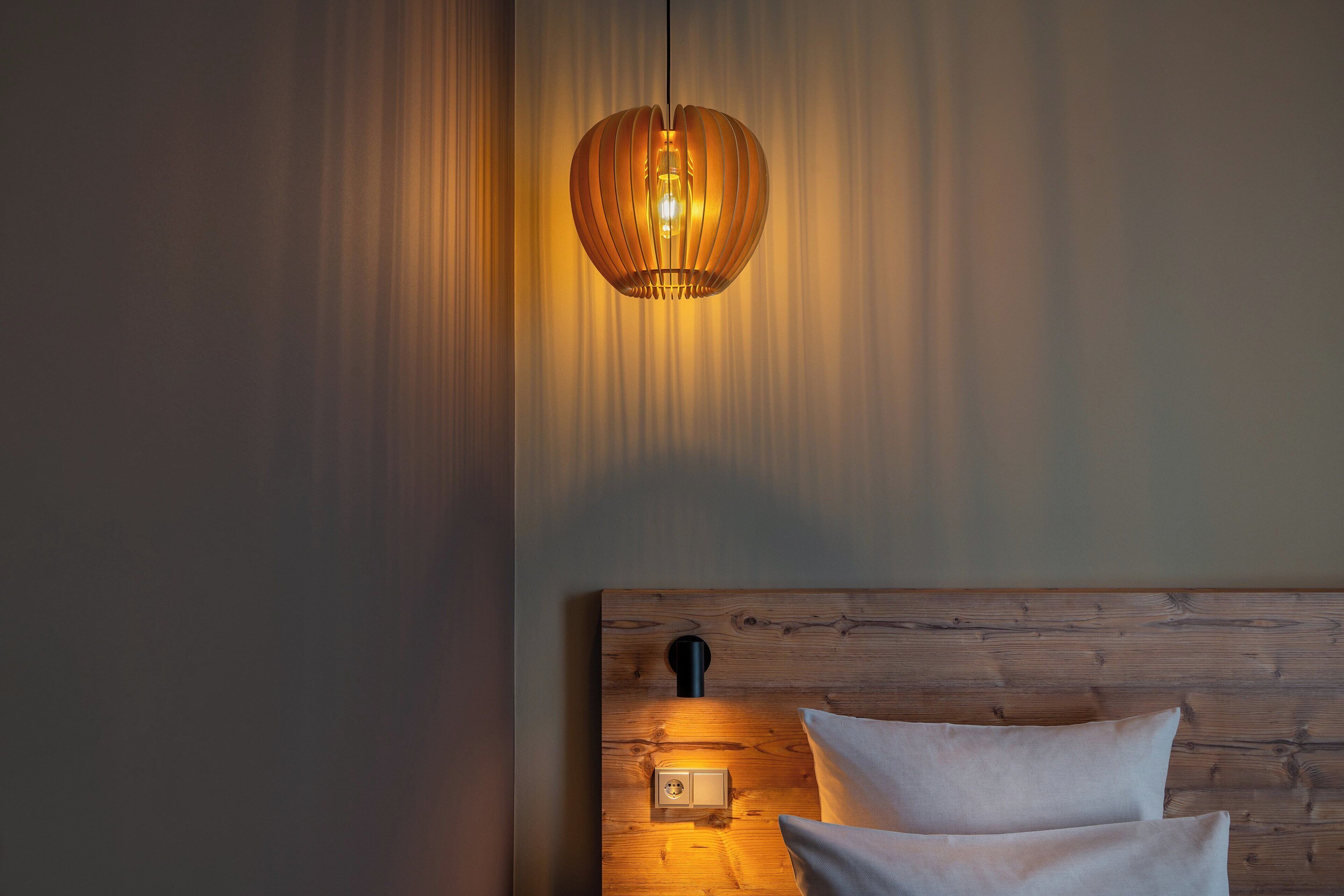 A bedroom with a wooden headboard, a bedside lamp, and a hanging light fixture.
