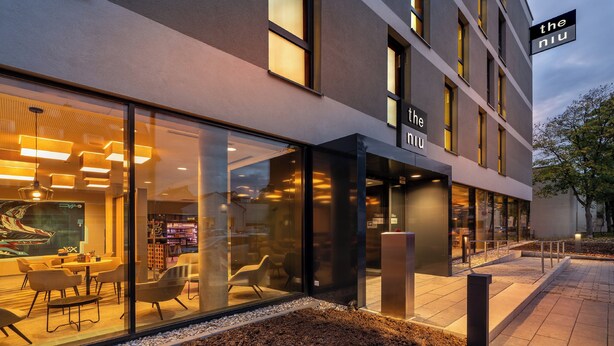 A modern building with a glass facade, a sign reading "the niu", and outdoor seating area. - Holiday Inn - the niu, Timber Esslingen by IHG (Esslingen)