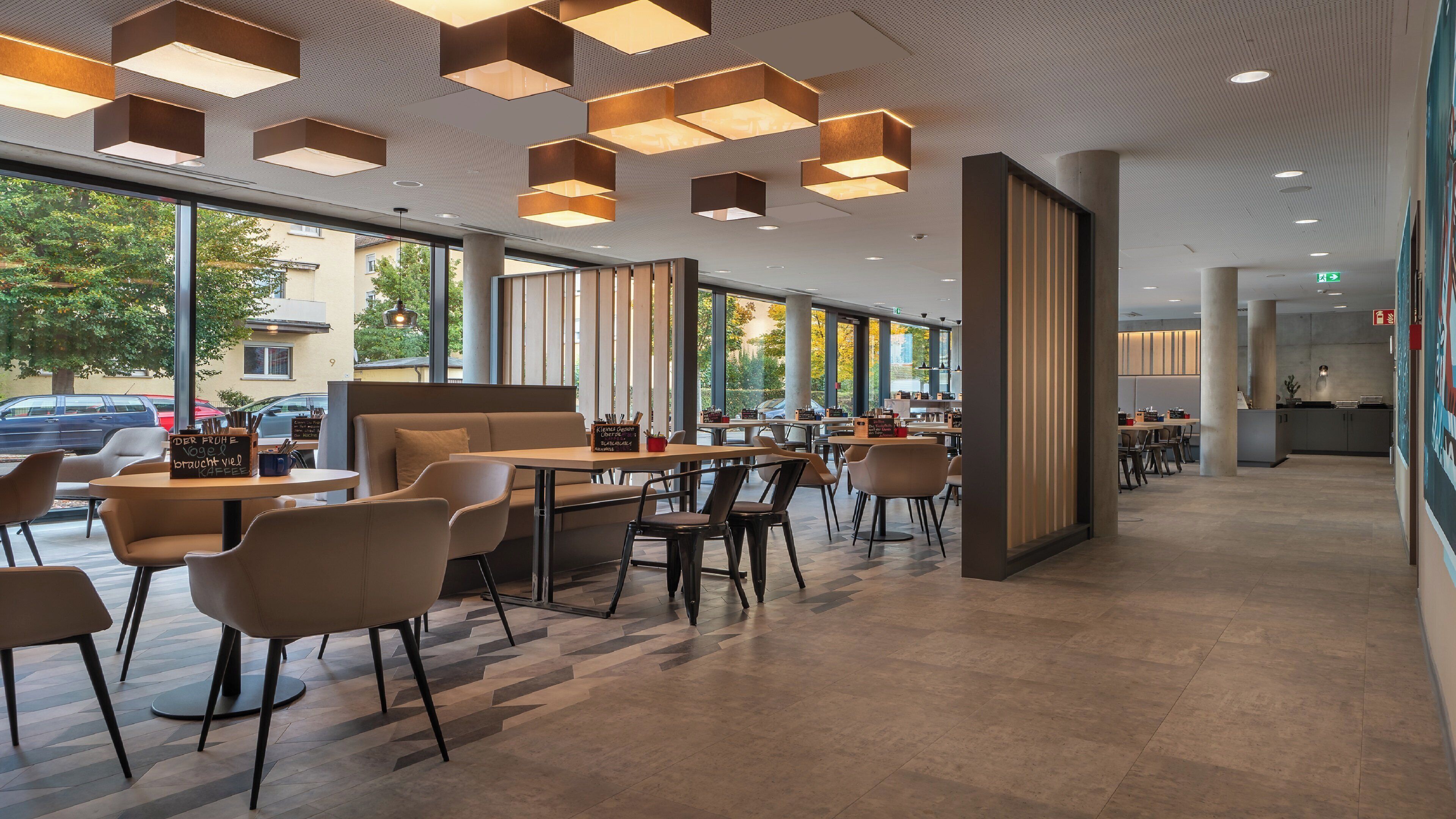 Un café moderne doté d’un espace salon central, de grandes fenêtres et d’un design contemporain au niveau du plafond.