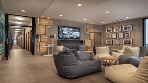 A modern lounge area with a large flat-screen TV, comfortable seating, and a hallway leading to elevators. - Holiday Inn - the niu, Timber Esslingen by IHG (Esslingen)