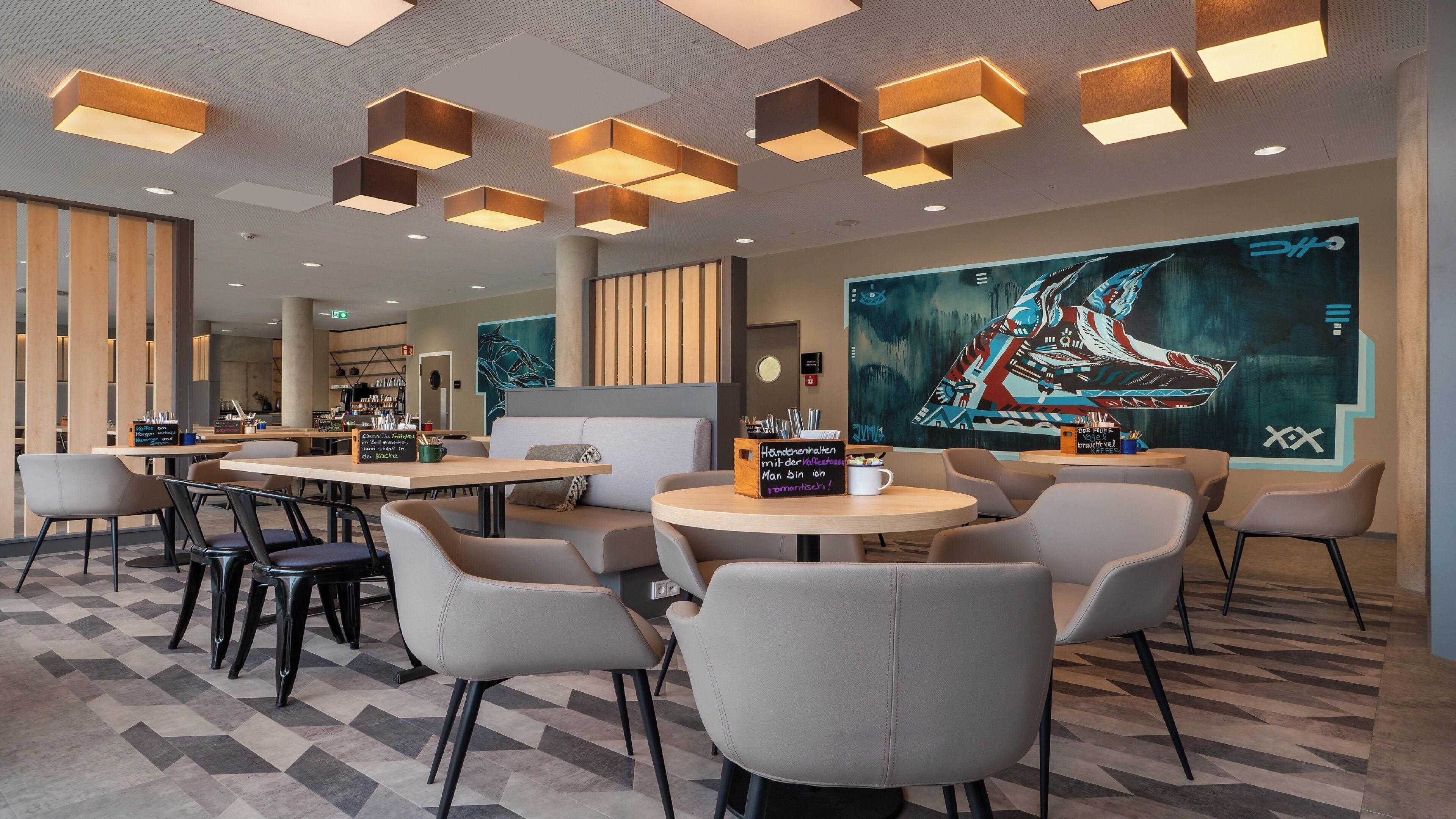 A modern cafe with round tables and chairs, a large digital art display, and a coffee bar in the background.