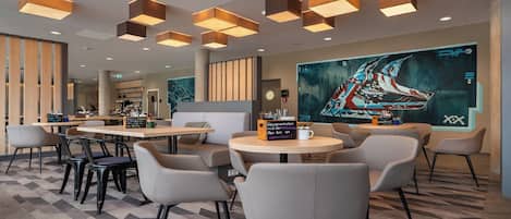 A modern cafe with round tables and chairs, a large digital art display, and a coffee bar in the background.