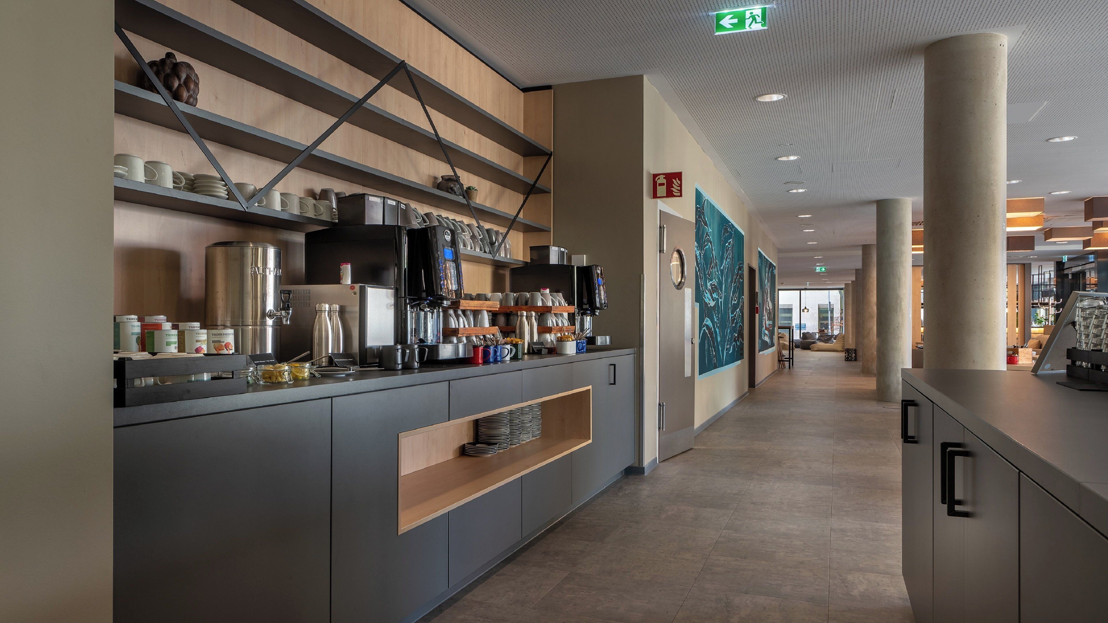 A modern hotel lobby with a long reception desk, wooden shelves, and a view into the dining area.
