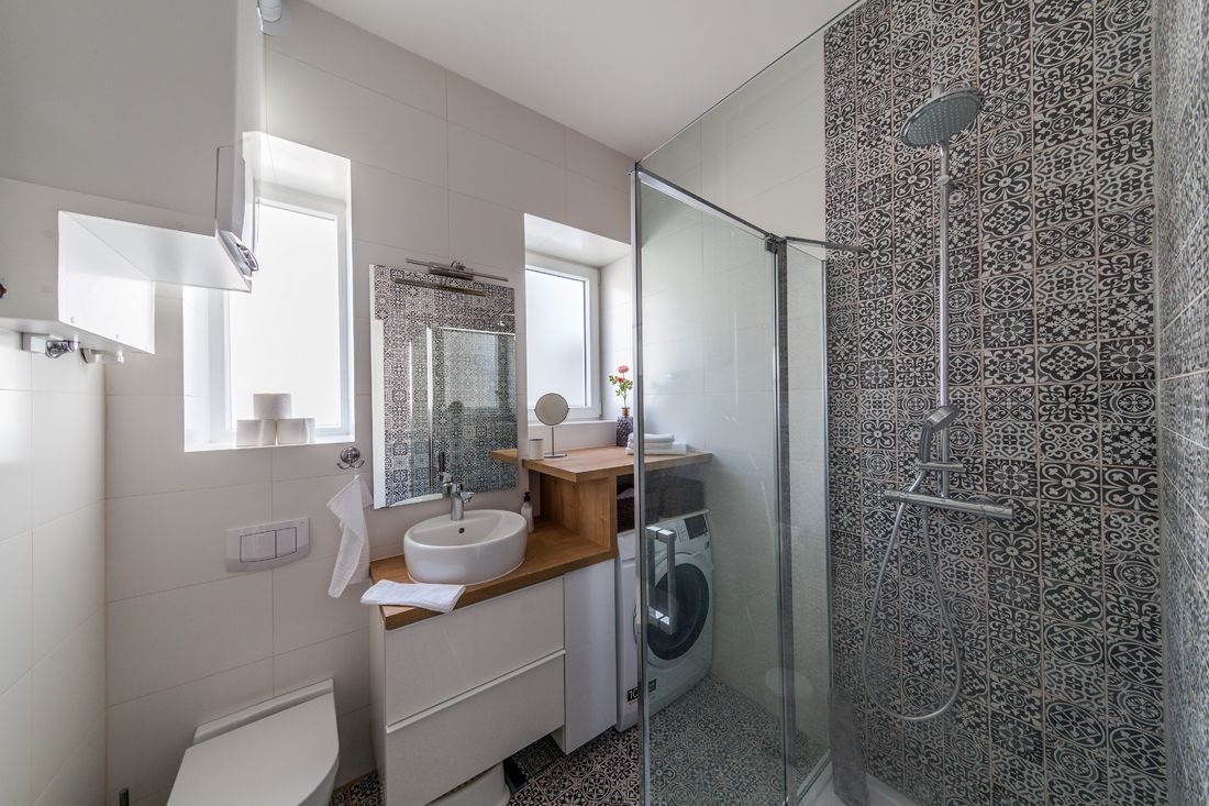 A modern bathroom with a glass shower enclosure, a built-in washing machine, and a large mirror above the sink.