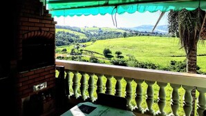 Un balcón con vistas a un paisaje verde, una chimenea de ladrillo y una planta colgante.