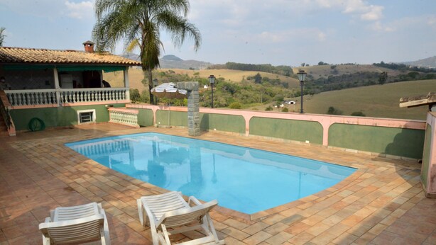 Una piscina con dos sillones de descanso, un porche cubierto y vistas a ondulantes colinas al fondo.