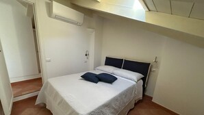 Un dormitorio pequeño y ordenado con una cama individual, una mesita de noche y un equipo de aire acondicionado instalado en la pared.