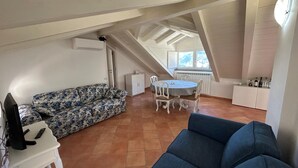 Un loft espacioso con techo alto, zona de comedor con sillas blancas, sofá floral y sofá azul.