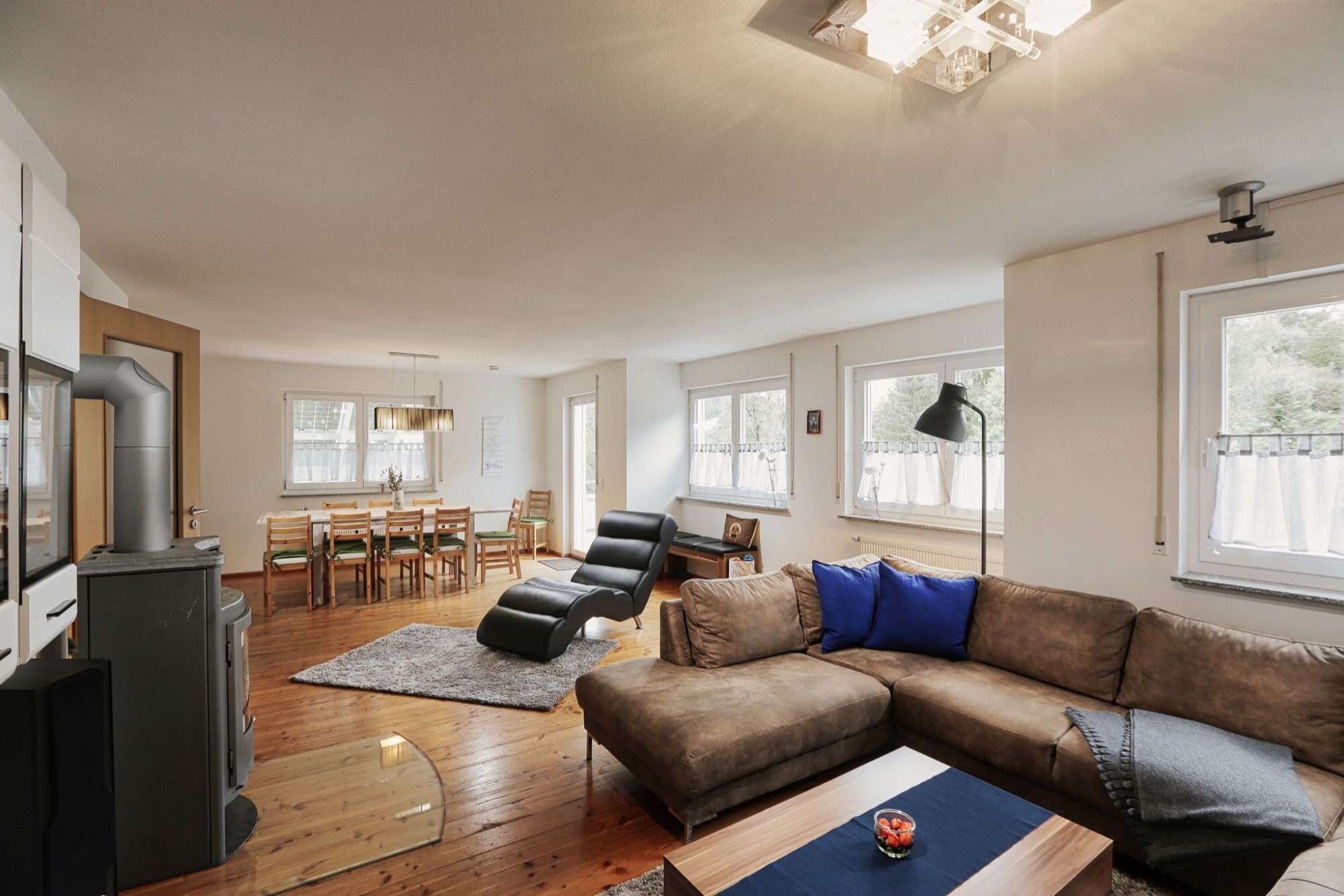 A spacious living room with a brown leather sofa, a dining area with wooden chairs, and a modern fireplace.